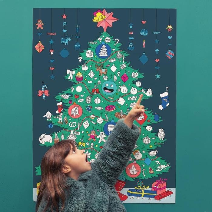 Uma criança a apontar para uma árvore de Natal decorada num poster gigante, com um fundo azul escuro.