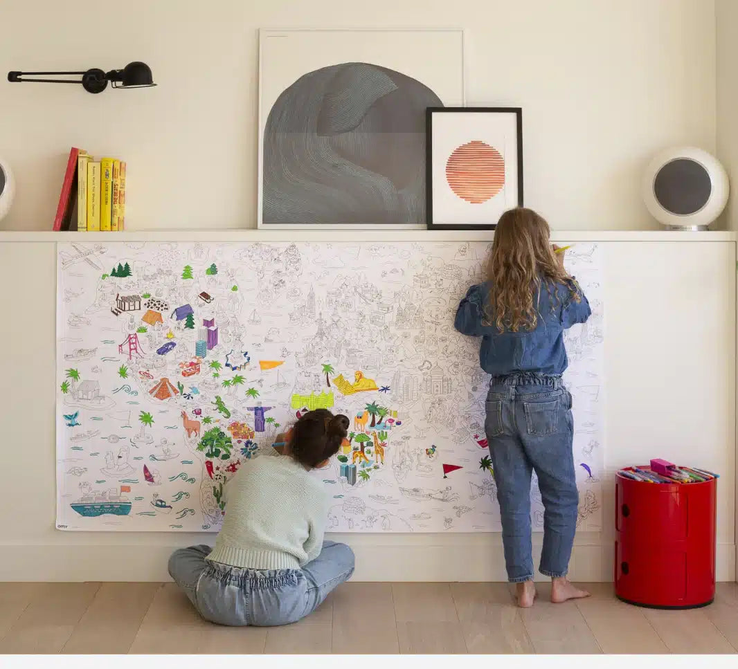 Duas meninas sentadas no chão a colorir um poster gigante da OMY com desenhos de todo o mundo.