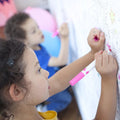 Uma menina a colorir um poster gigante da OMY com um marcador rosa.