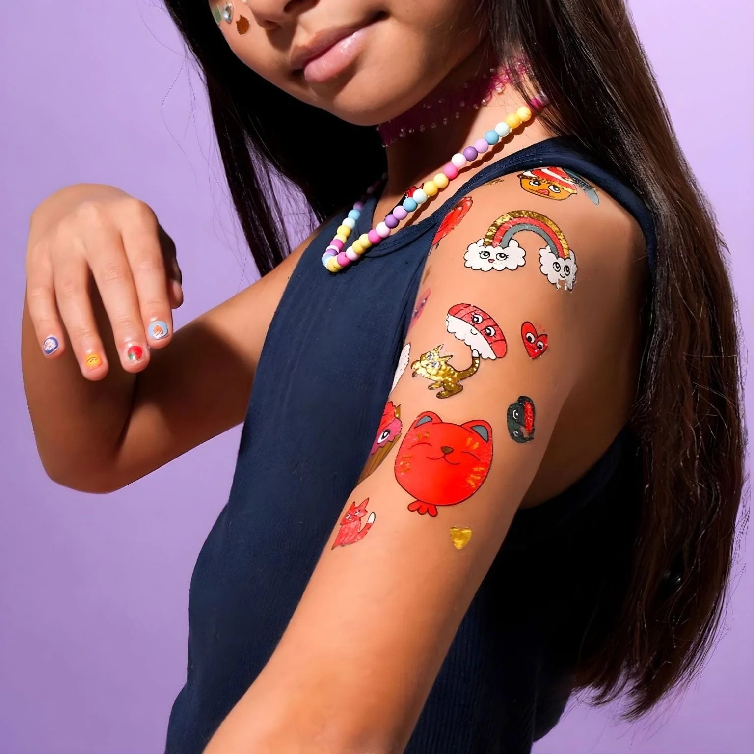 Criança com cabelo comprido a exibir tatuagens temporárias OMY Kawai aplicadas no braço, incluindo um gato vermelho, arco-íris e cogumelo.