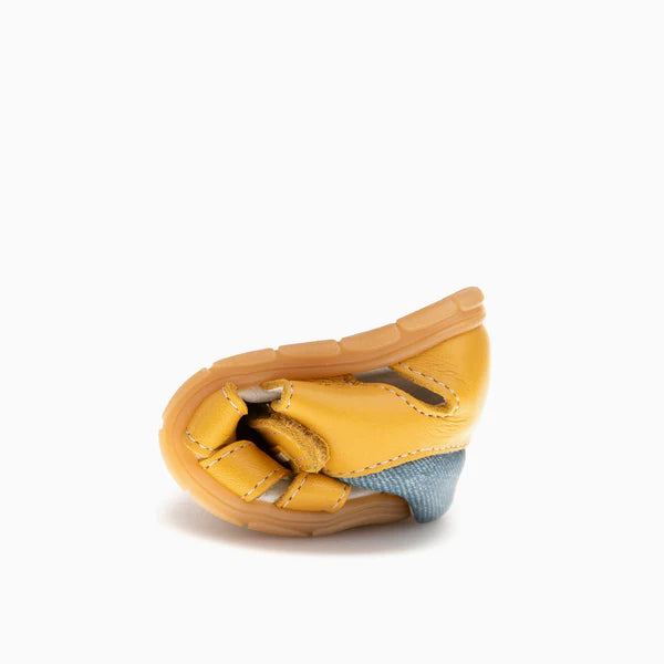 Demonstração da flexibilidade da sandália barefoot Pablosky Savana Tuorlo amarela, dobrada sobre si mesma, destacando a sola fina e o forro em ganga.