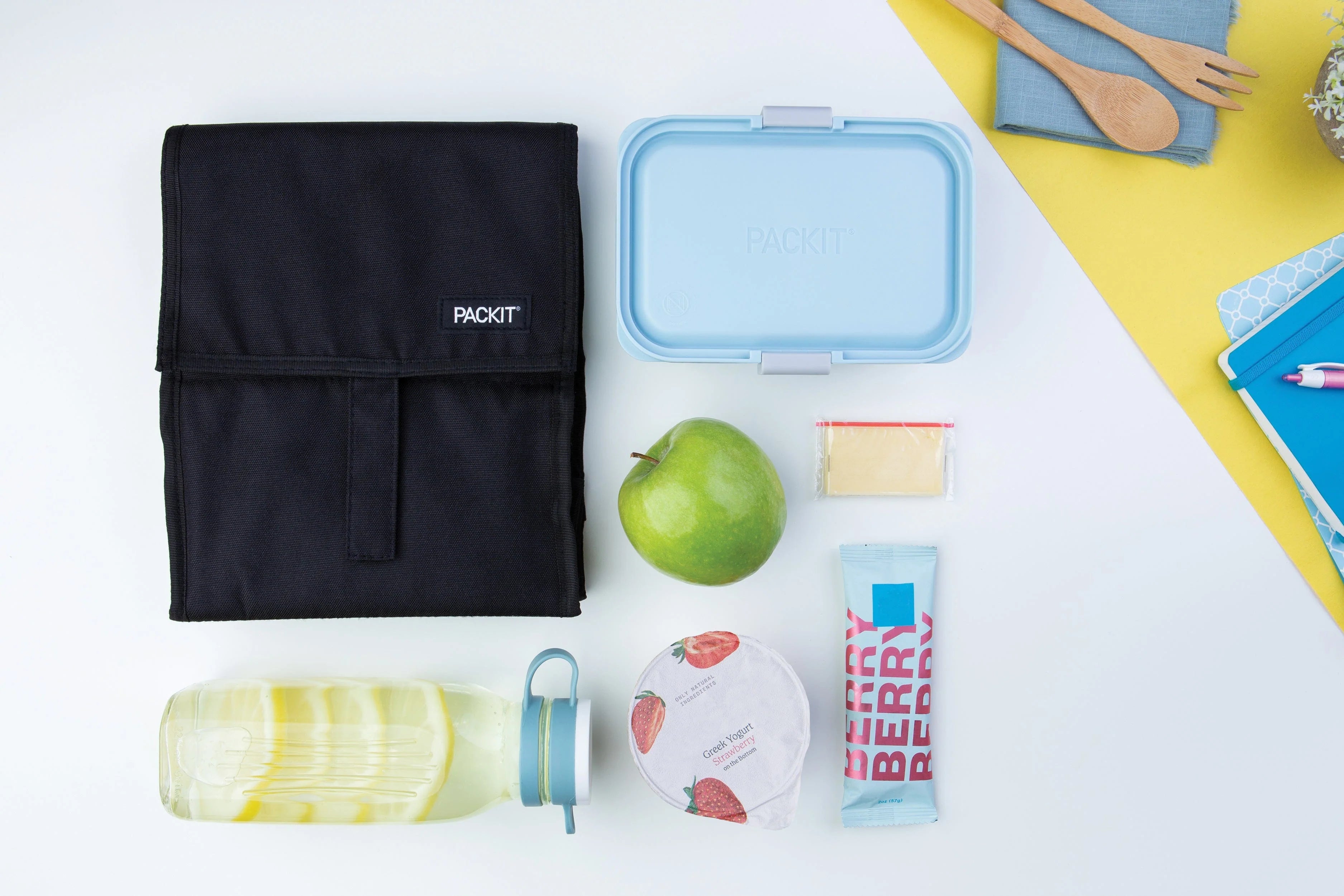 Packit Bolsa lancheira térmica preta aberta, mostrando o seu interior espaçoso com um recipiente azul, maçã verde, iogurte, bebida e snacks, pronta para ser usada.