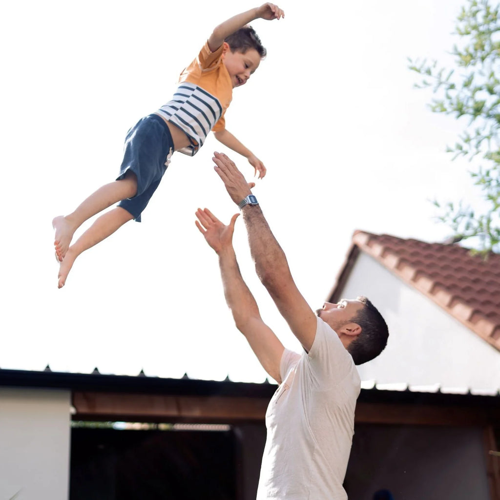 Pai a atirar o filho para o ar, o menino usa a t-shirt de segurança Floatee amarela, demonstrando liberdade de movimento e diversão.