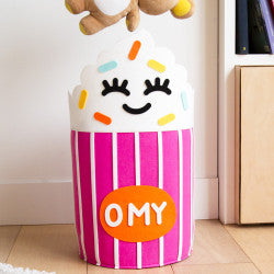 Close-up do OMY Cesto de Arrumação em forma de cupcake rosa com detalhes de cobertura branca e granulado colorido, num ambiente interior.