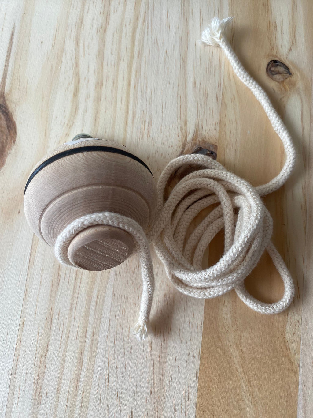 Pião de madeira natural com cordão branco enrolado, pronto a lançar, sobre uma superfície de madeira clara.