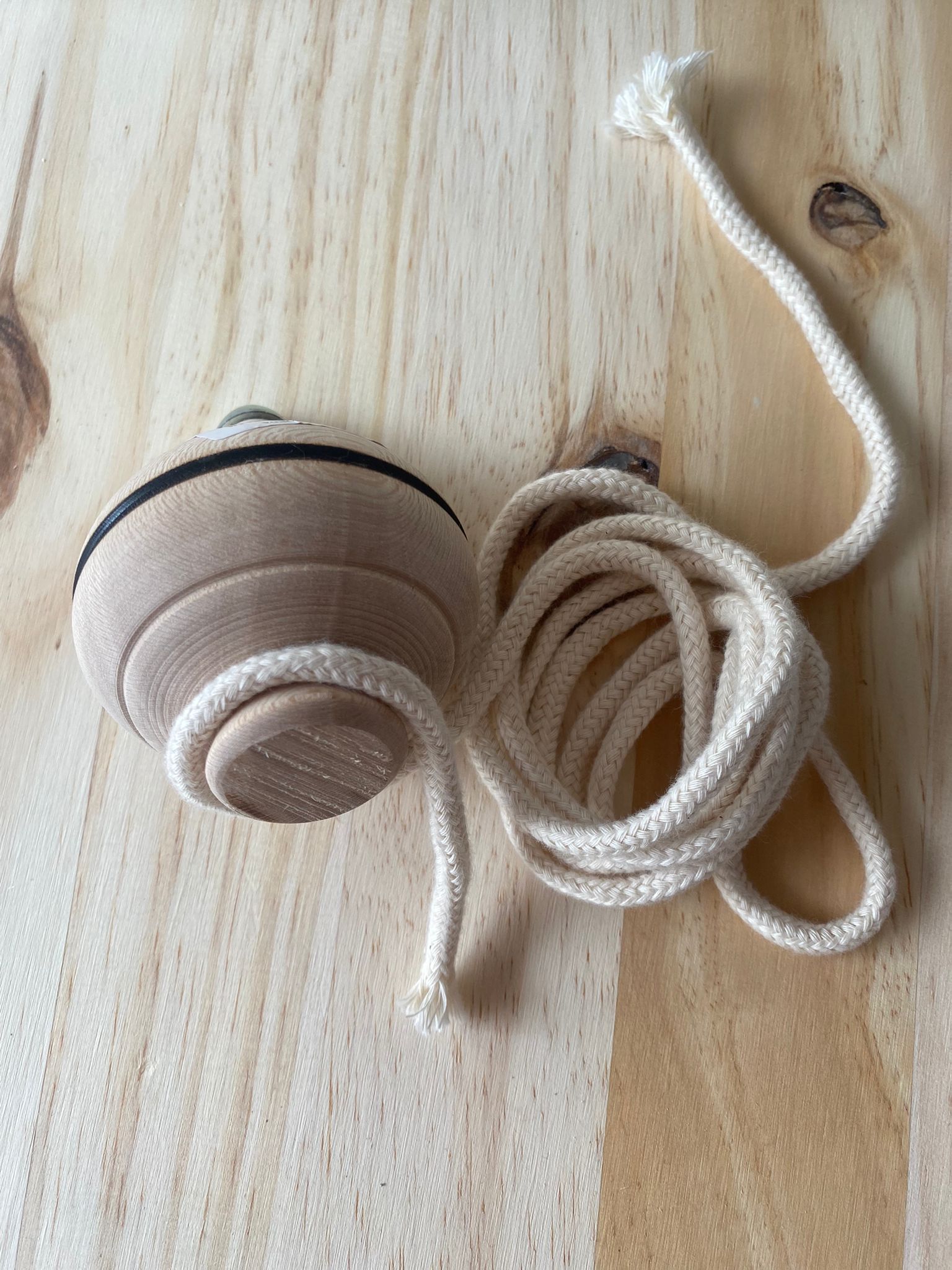 Pião de madeira natural com cordão branco enrolado, pronto a lançar, sobre uma superfície de madeira clara.