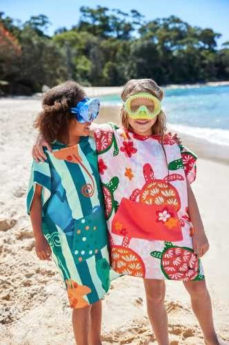 Crianças felizes na praia a usar ponchos de secagem rápida Dock and Bay às riscas coloridas.