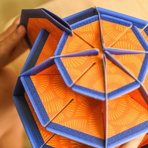 Detalhe da montagem do Globo Poppik, mostrando peças de cartão laranja e azul a serem encaixadas sem cola.