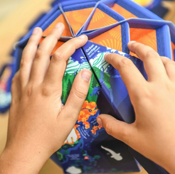 Mãos de criança a montar o Globo Mundo 3D Poppik, encaixando peças com o Oceano Ártico visível.