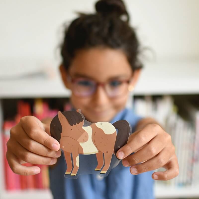 Criança com óculos a segurar um autocolante grande de pónei castanho e branco do kit Poppik, mostrando a qualidade do adesivo reposicionável.