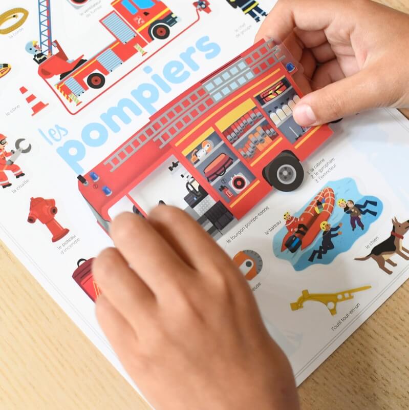 Criança a interagir com o poster educativo Poppik Bombeiros, colando um autocolante de um camião de bombeiros aberto, revelando os compartimentos internos.