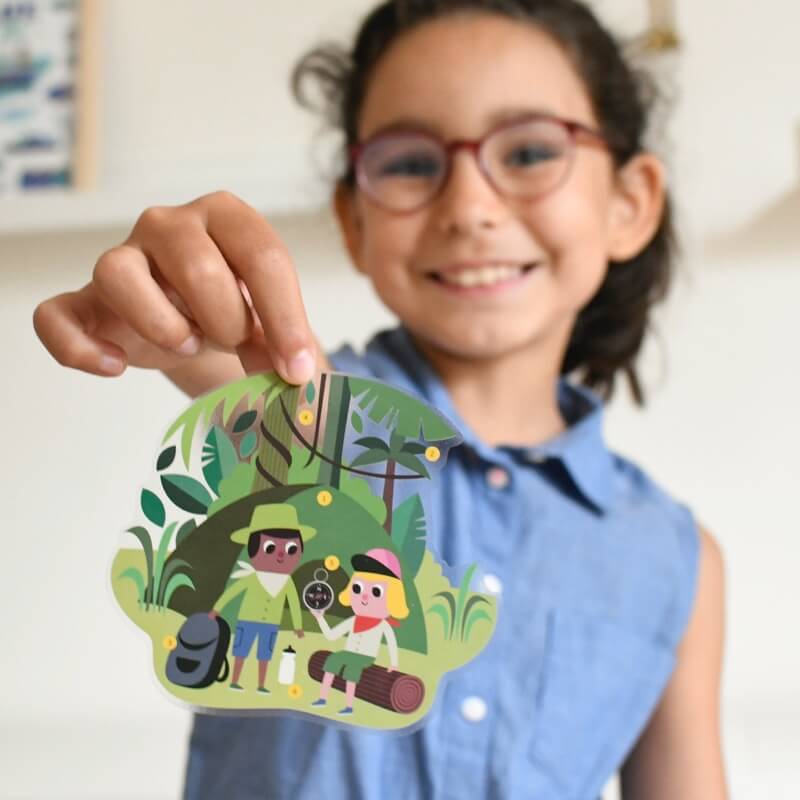 Criança sorridente com óculos a segurar um autocolante grande do poster Poppik Jungle, mostrando dois exploradores no cenário da selva.