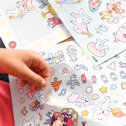 Detalhe de mãos de criança a aplicar um autocolante de pássaro no poster Poppik Party, mostrando a folha de autocolantes com figuras kawaii.