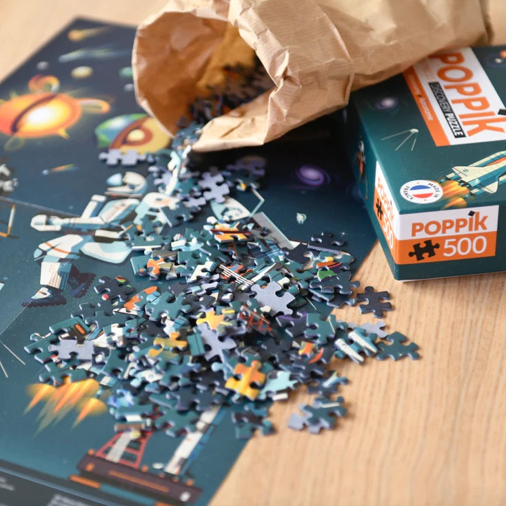 Peças do puzzle Poppik Astronomy a serem despejadas de um saco de papel sobre o poster parcialmente montado na mesa.