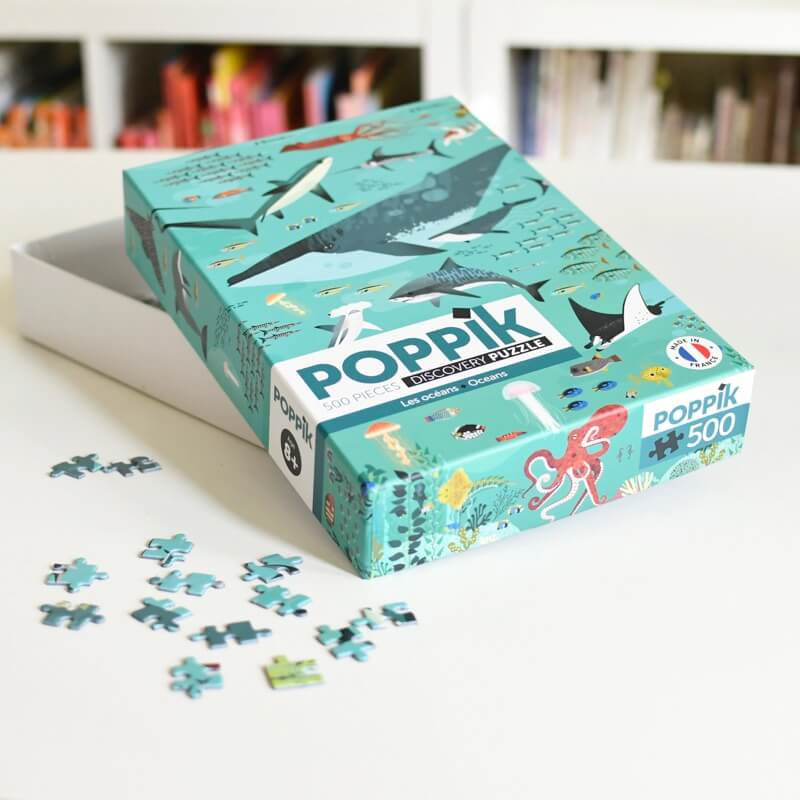 Caixa do puzzle Poppik Ocean 500 peças pousada numa mesa branca, com algumas peças soltas espalhadas em frente, em ambiente de sala iluminada.