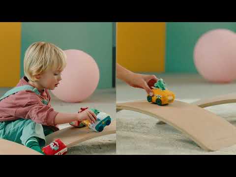 Criança brincando com carrinhos de tecido Lilliputiens em tábua de equilíbrio. Mostra uso e movimento do brinquedo.