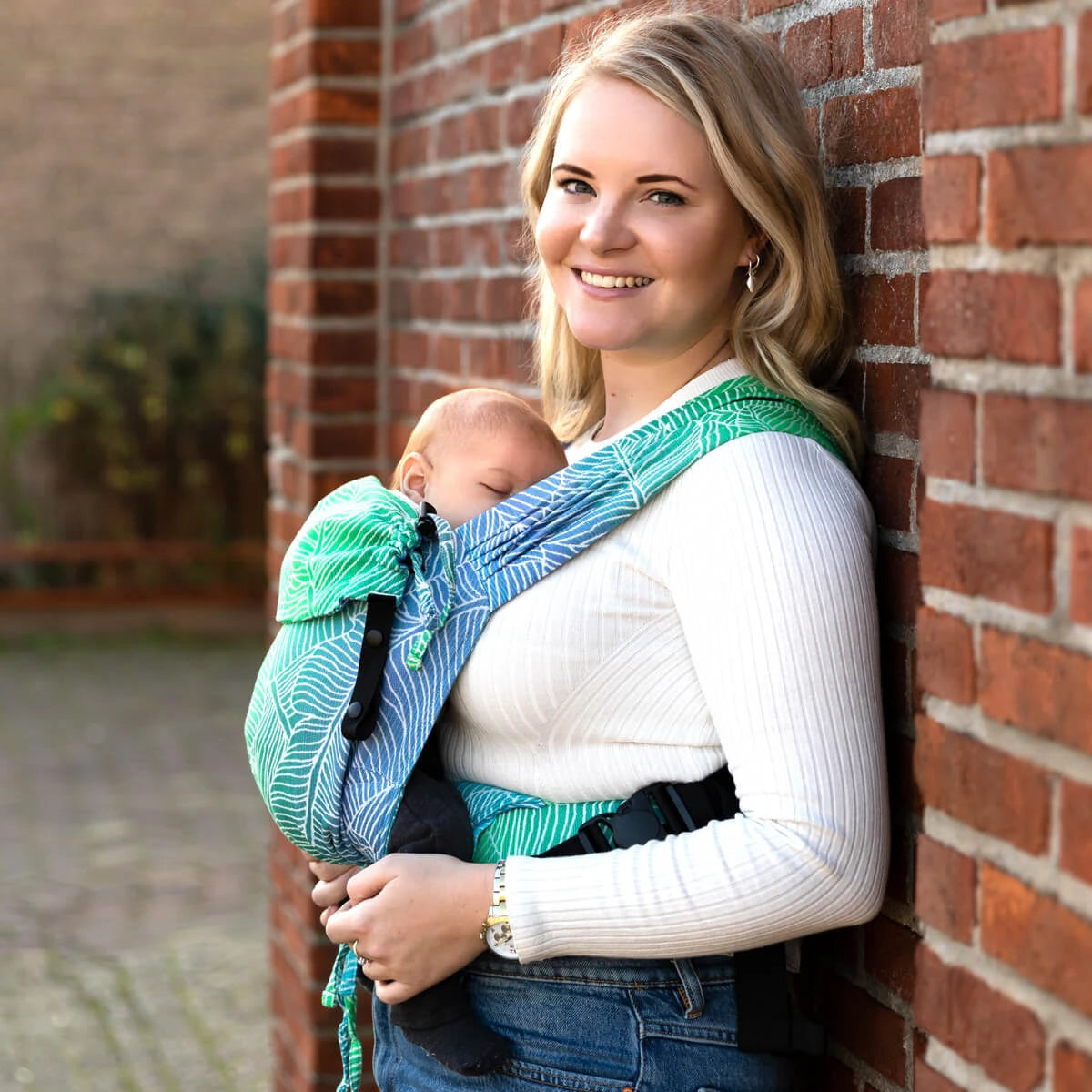 Mulher sorridente com bebé na mochila Primeo, destacando o porte à frente.