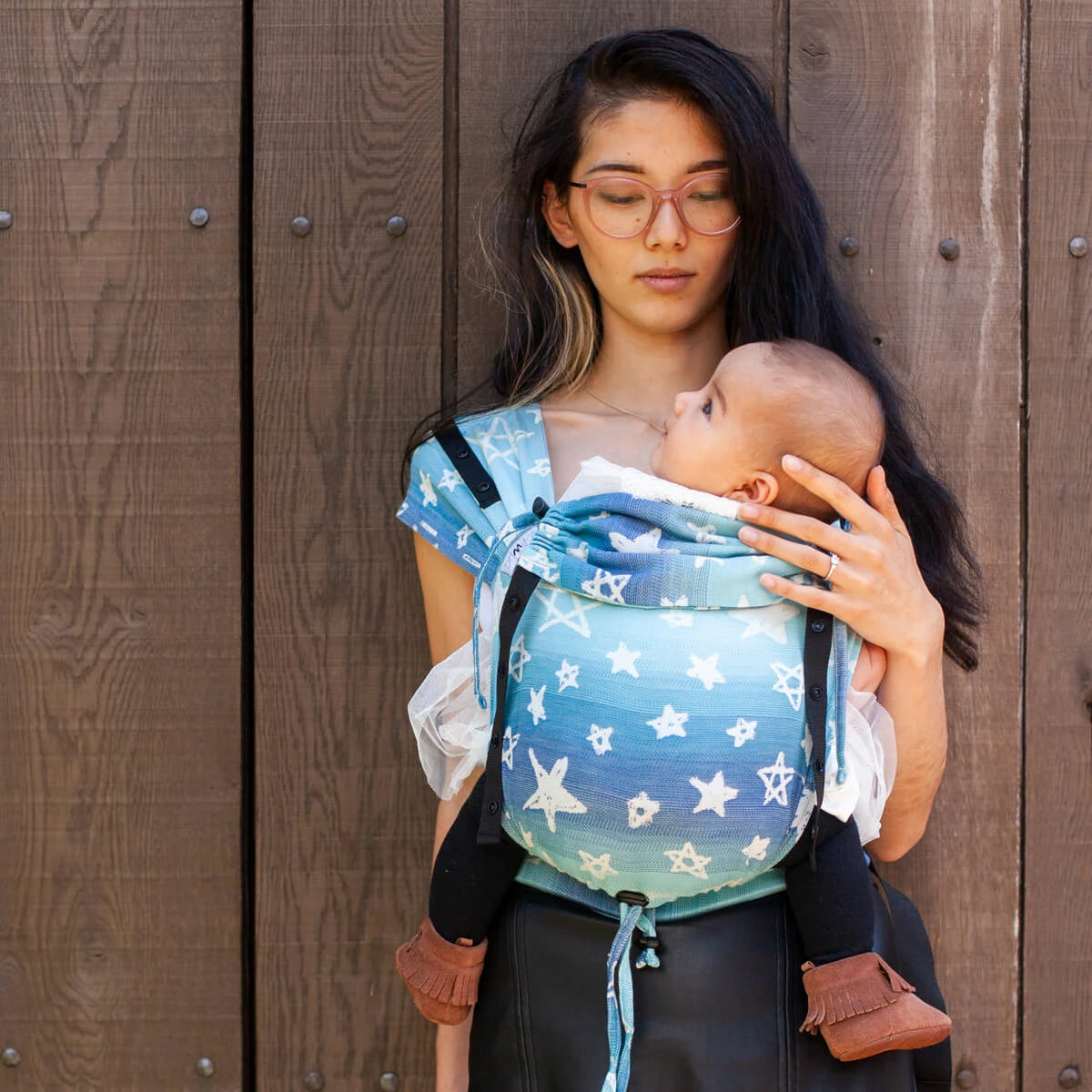 Mulher a usar a mochila Hoppediz Primeo Singapor Blue com um bebé, mostrando o ajuste frontal.