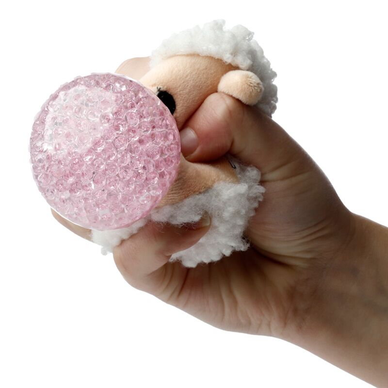 Uma mão a apertar um brinquedo Queasy Squeezies Adoramals em forma de ovelha, mostrando a bola espremível rosa no interior.