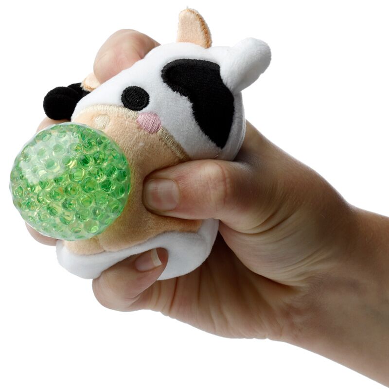 Uma mão a apertar um brinquedo Queasy Squeezies Adoramals em forma de vaca, mostrando a bola espremível verde no interior.