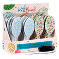Expositor de cartão com várias escovas de cabelo Puckator "Pick of the Bunch", incluindo modelos com padrão de margaridas azuis e florais coloridos. Uma escova está em primeiro plano.