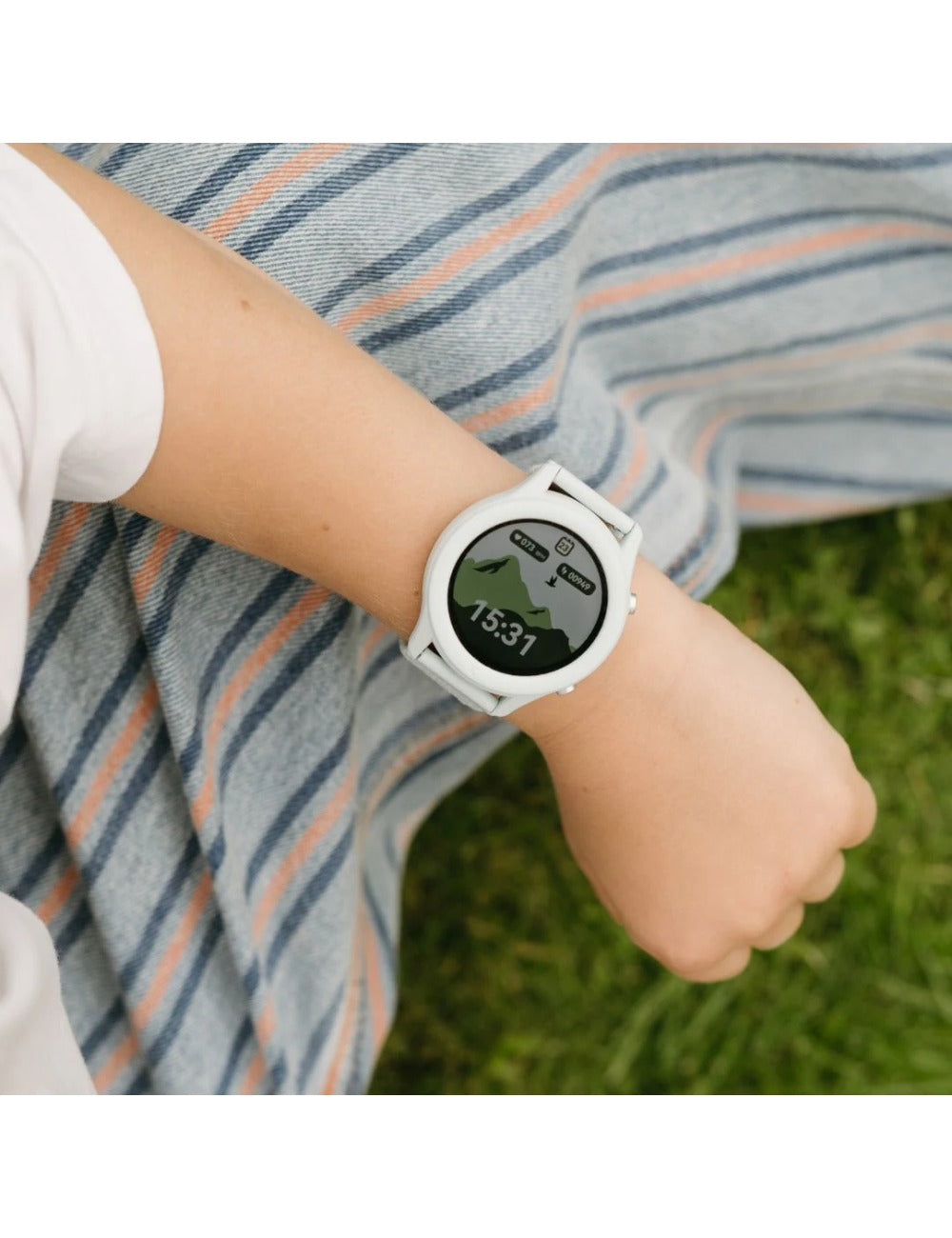 Detalhe do pulso de uma criança a usar o relógio KidyWolf K-watch, com o mostrador a exibir a hora (15:31) e um ícone de montanha.