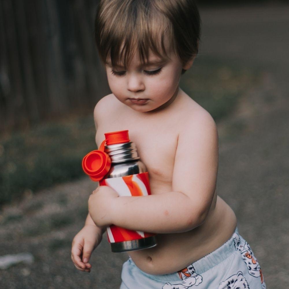 Garrafa Pura Sport 550ml em aço inoxidável com capa azul sobre uma mesa de madeira num ambiente doméstico.