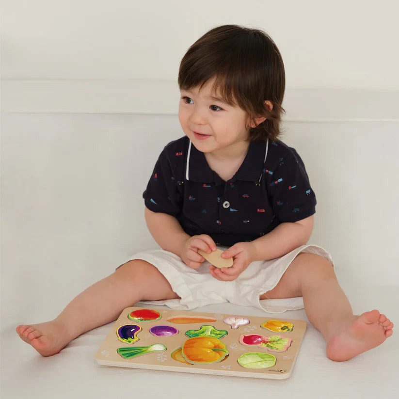 Criança sentada a brincar com o Classic World Puzzle de encaixe Vegetais, mostrando a interação com o brinquedo.