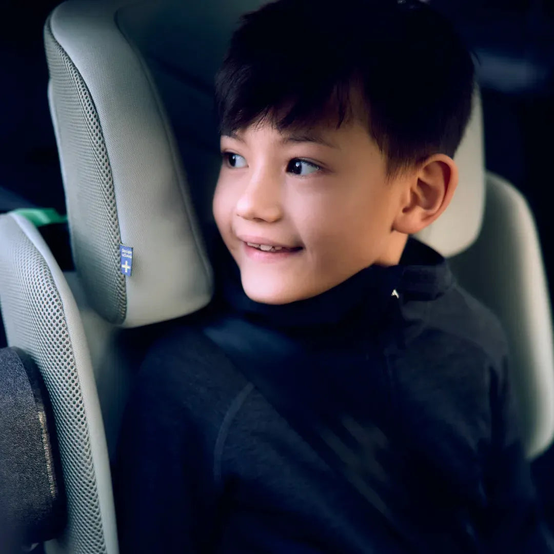 Close-up de um rapaz sorridente sentado na cadeira auto Axkid Up, mostrando o conforto e o ajuste do apoio de cabeça.