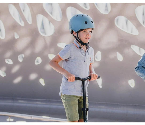 Criança a andar de trotinete com capacete Scoot & Ride azul 45-51cm (2-5 anos) para segurança.