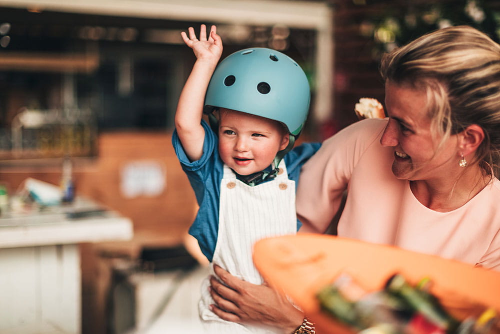 Criança feliz com capacete Scoot & Ride azul 45-51cm (2-5 anos) ao lado de um adulto.