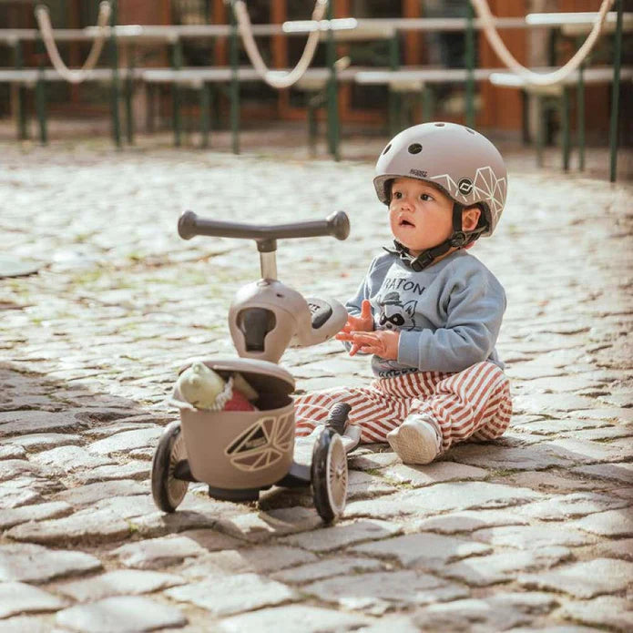 Criança pequena com capacete a usar a Highwaykick 1 Lifestyle em modo triciclo no exterior, promovendo o desenvolvimento motor.
