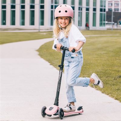 Criança sorridente a andar de trotinete rosa Scoot & Ride com luzes LED, em passeio exterior.