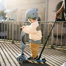 Criança pequena a usar a trotinete Scoot & Ride em pé, com um adulto a empurrar através da barra parental ajustável.