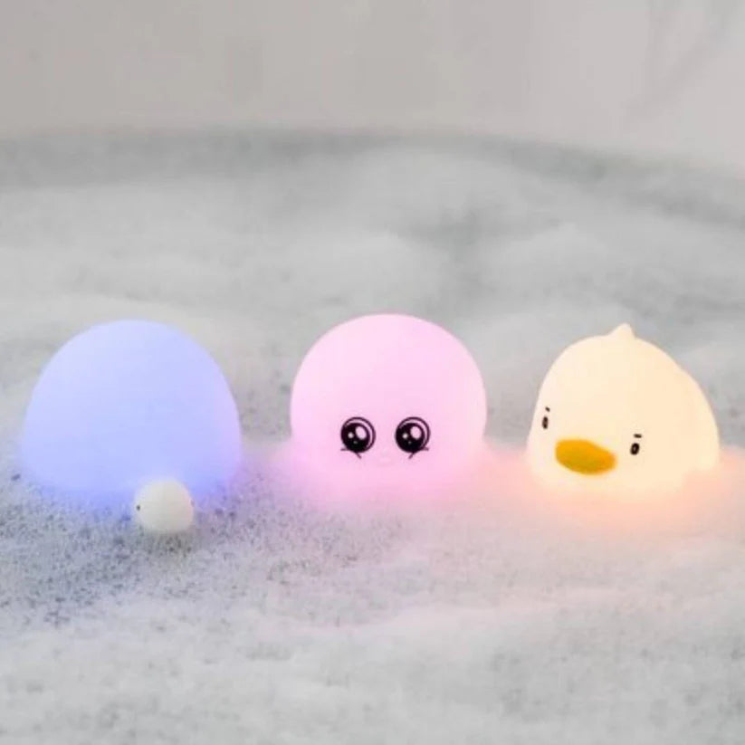 Três lâmpadas Rabbit e Friends (tartaruga, polvo, patinho) a brilhar com cores diferentes em água com espuma, criando um ambiente mágico no banho.