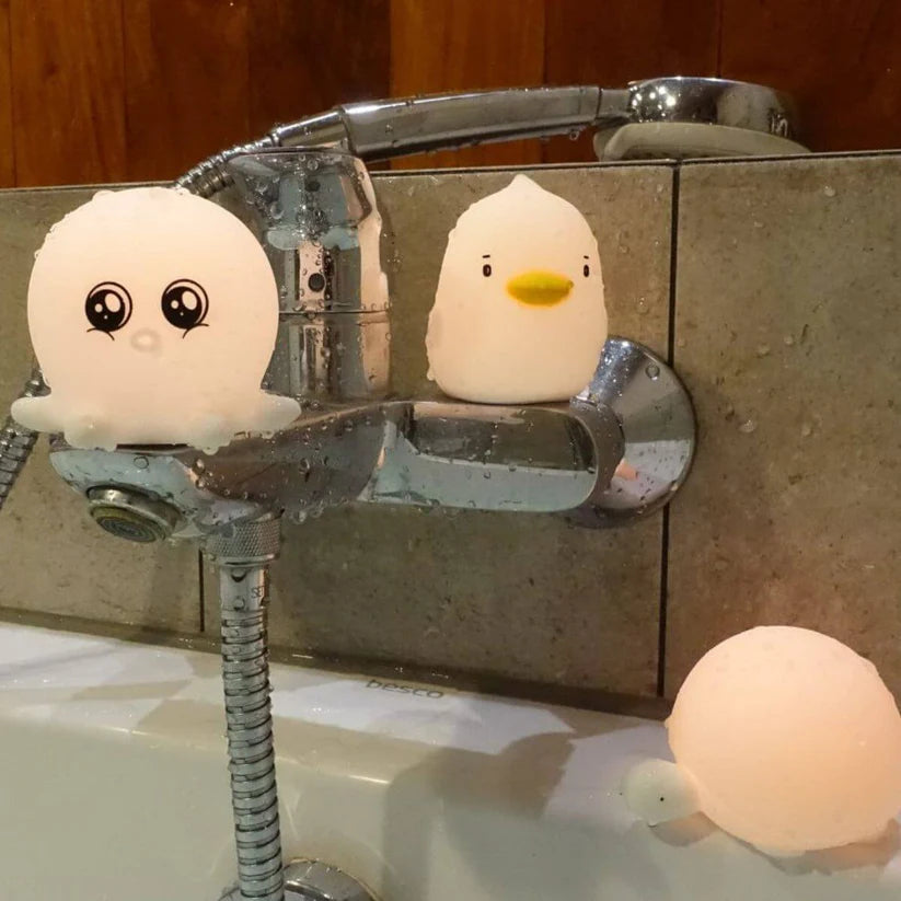 Duas lâmpadas Rabbit e Friends (polvo e patinho) acesas e com gotas de água numa torneira de banheira, com a lâmpada tartaruga acesa no lavatório.