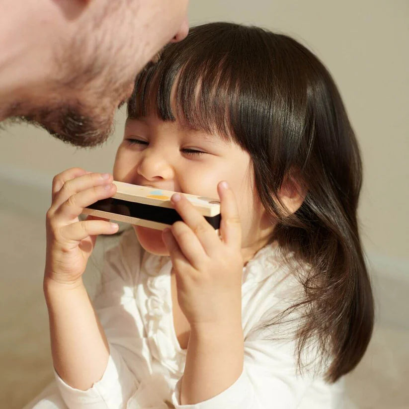 Close-up de um adulto e uma criança pequena a brincar com um instrumento musical de sopro, sorrindo e interagindo.