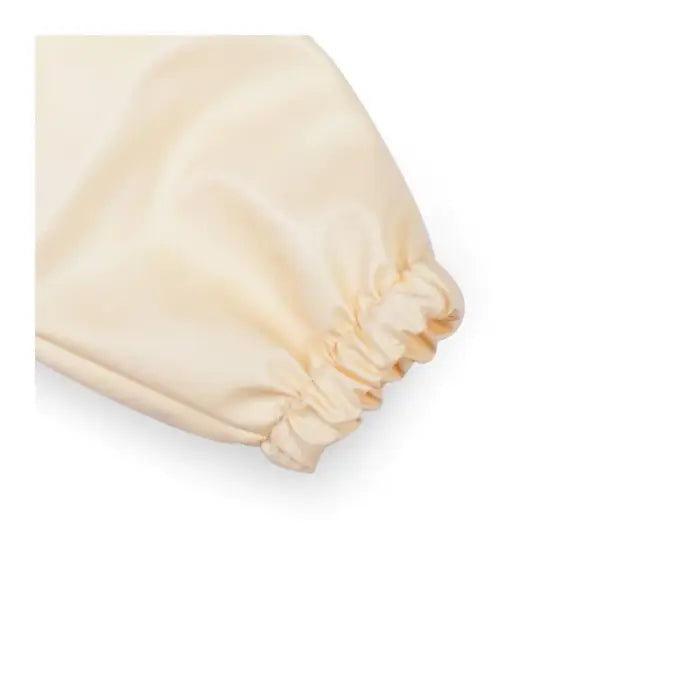 Detalhe do punho elástico da manga do babete Miniland creme, demonstrando a barreira contra líquidos e alimentos.