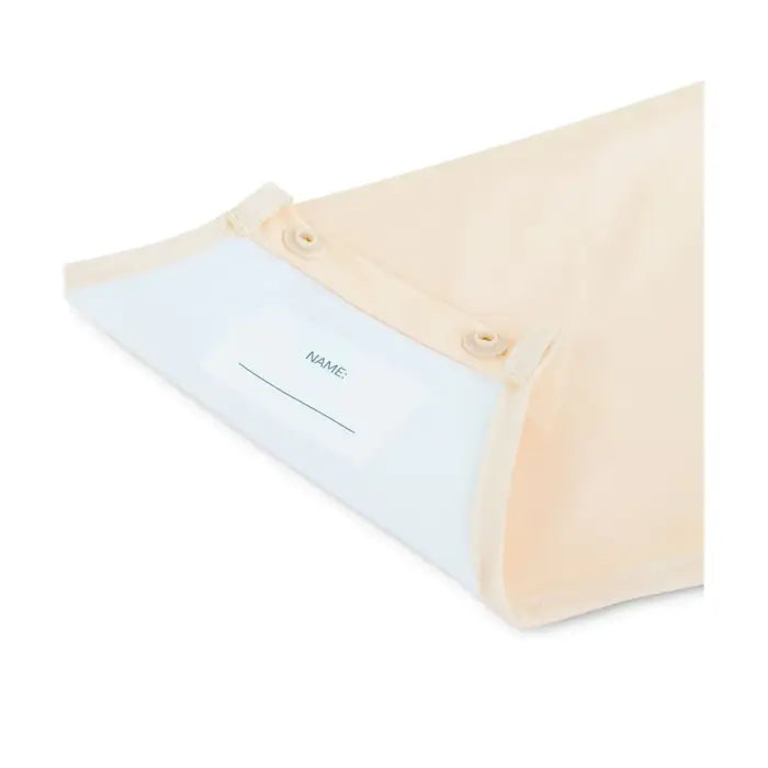 Vista aproximada da etiqueta personalizável "NAME:" no interior do babete Miniland, junto ao fecho de pressão.