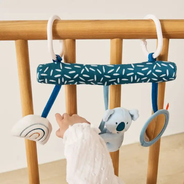 Bebé a interagir com a Miniland Espiral do Coala pendurada num berço de madeira, esticando a mão para o coala.