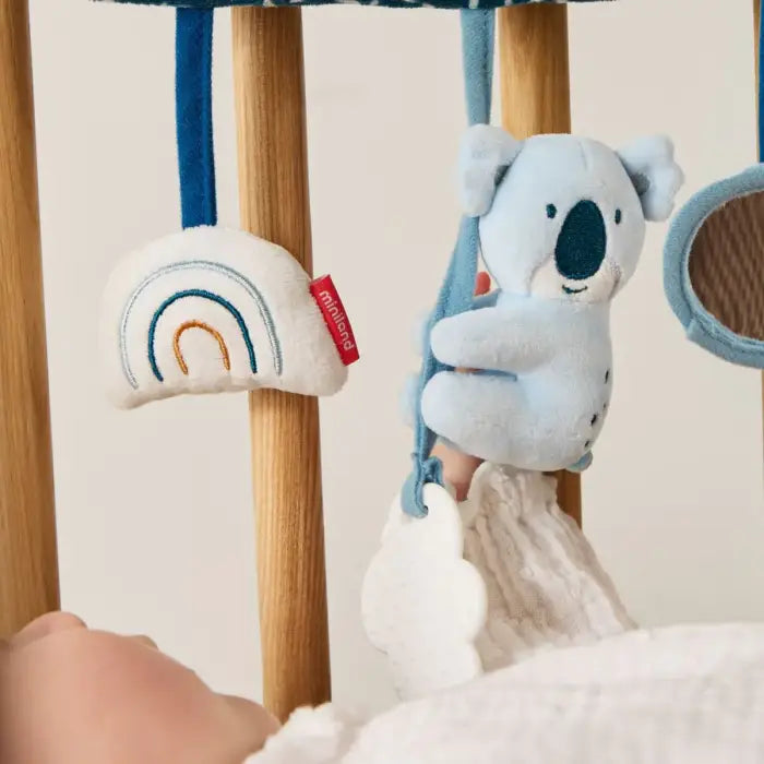 Detalhe da Miniland Espiral do Coala no berço, mostrando o coala, o mordedor e o arco-íris de perto com a mão do bebé.