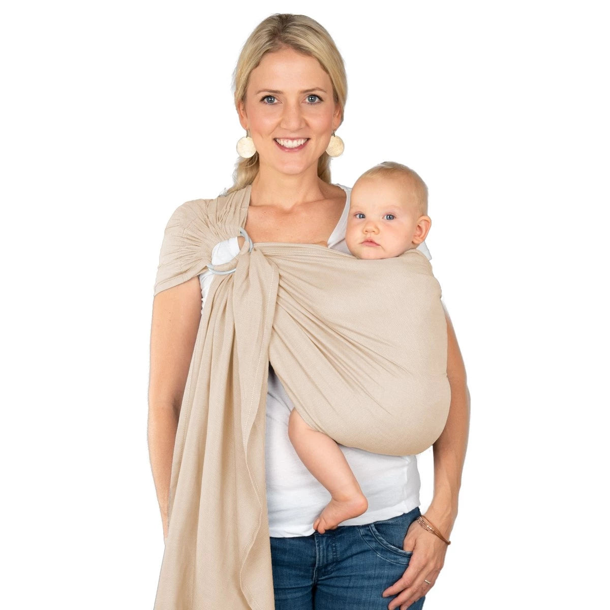 Mulher sorridente a carregar um bebe num sling de argolas Hoppediz Hamburg de cor bege frappe.