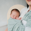 Bebé recém-nascido a dormir pacificamente no Sling de Argolas Neobulle Jersey Tilleul, cor verde-água, junto ao peito da mãe.