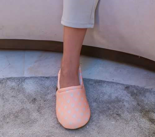 Pé de criança a usar a pantufa Slip Stop Booties cor de rosa claro com corações, em cima de um tapete cinzento, demonstrando o uso interior.