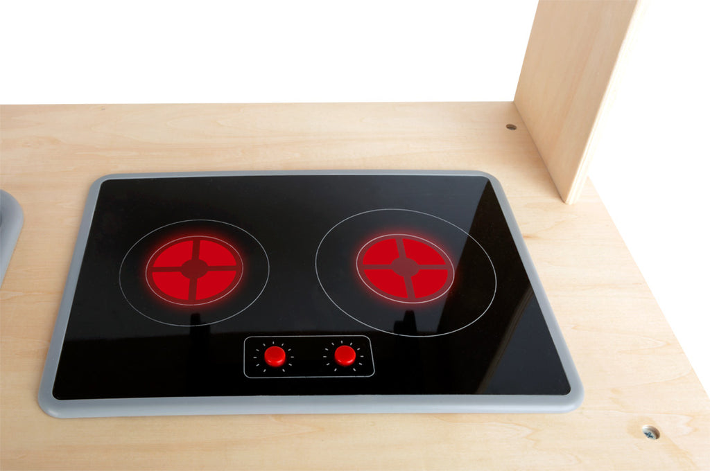 Foco no fogão de brincar com duas placas pretas e botões vermelhos simulando aquecimento (brilho vermelho).