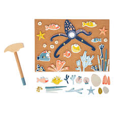 Vista geral do jogo de martelar Small Foot, mostrando o martelo de madeira separado do painel de cortiça com figuras marinhas e peças soltas em primeiro plano.