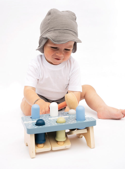Criança pequena com gorro cinzento a brincar com o jogo de martelar de madeira "Sobe e Desce Ártico" da Small Foot.