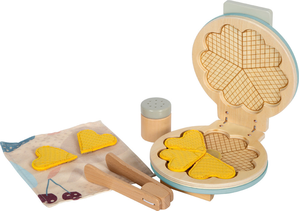 Máquina de waffles de brincar em madeira aberta, mostrando os waffles de coração amarelos no interior e acessórios como pinça e doseador de açúcar.