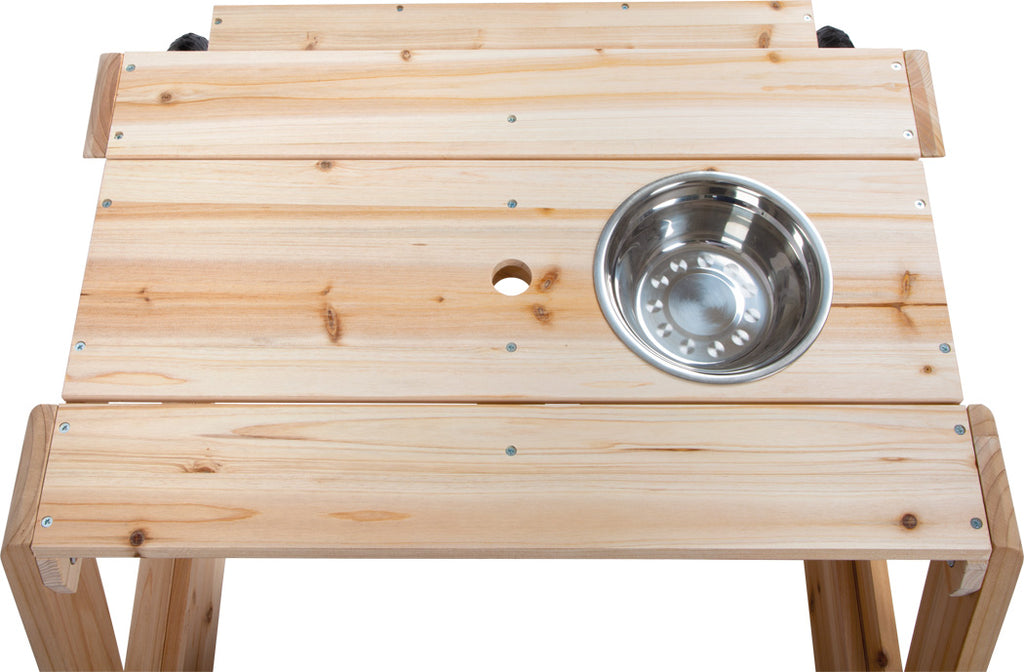 Detalhe do tampo de madeira da mesa de brincar, exibindo a taça de metal amovível e o orifício central para acessórios como um guarda-sol.