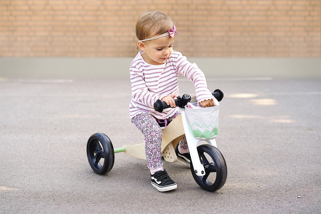 Criança pequena sentada no triciclo de treino Small Foot, concentrada, com o veículo configurado como triciclo.